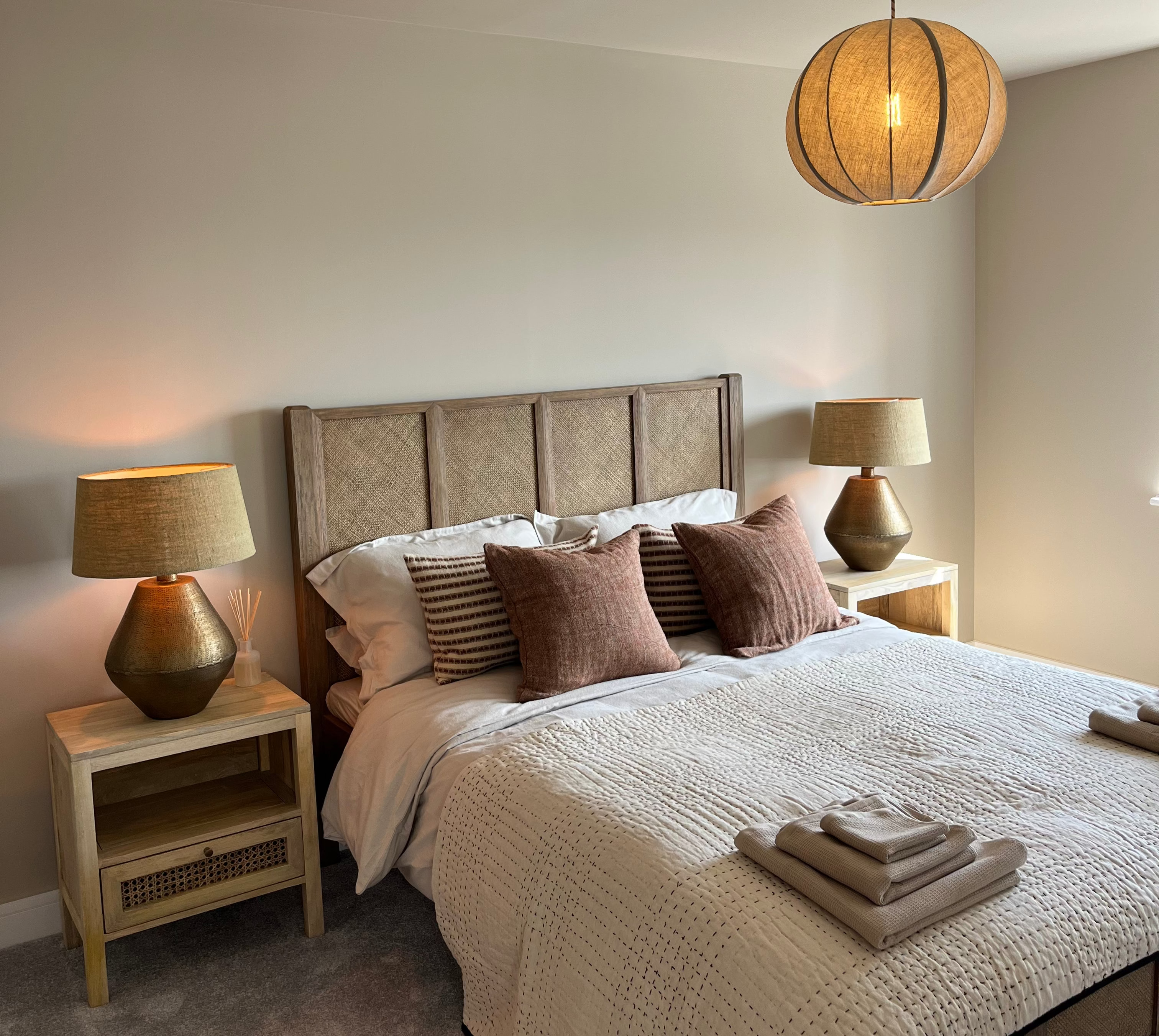 Neatly made bed with decorative pillows in a bedroom setting with lamps on wooden bedside tables.