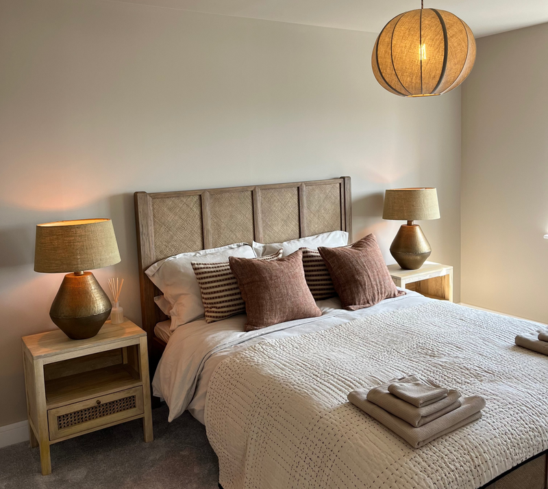 Neatly made bed with decorative pillows in a bedroom setting with lamps on wooden bedside tables.