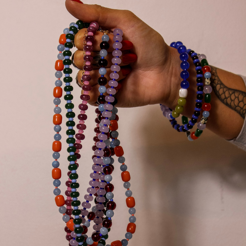 Hand holding colorful beaded necklaces against a plain background