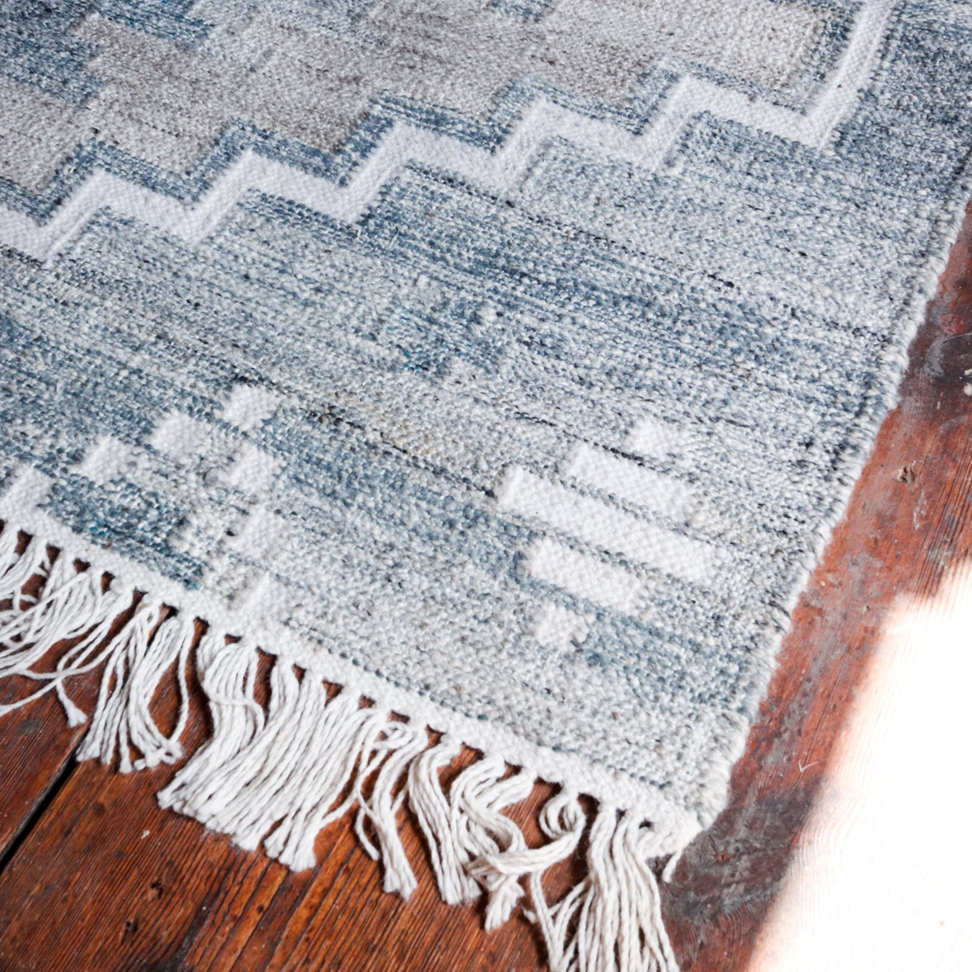Large Blue & Cream Geometric Recycled Plastic Rug Blue Rug with white tassels on dark wooden floor 