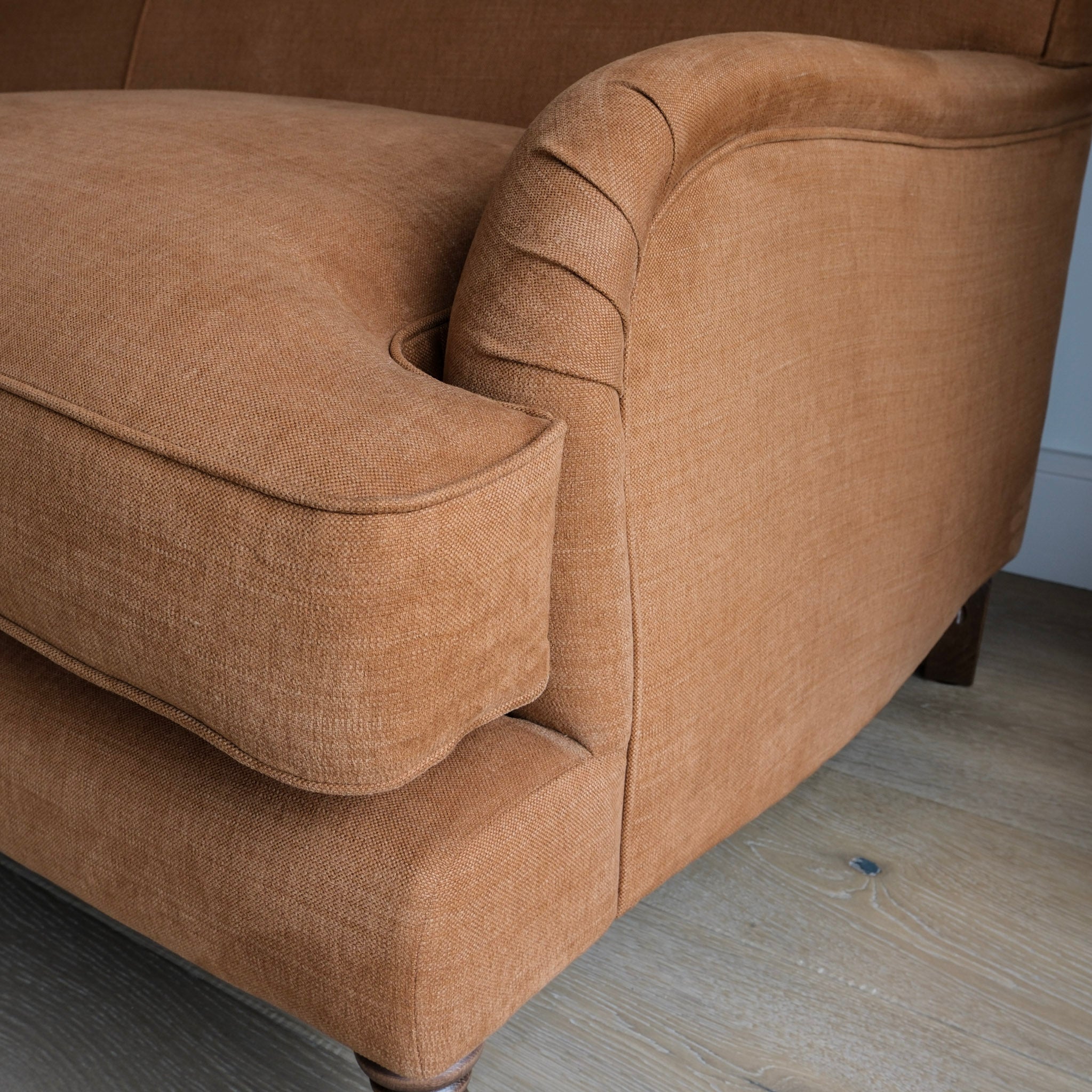 Close-up of a chocolate cotton linen textured fabric armchair showing the cushion, armrest, and wooden legs on a light wood floor.