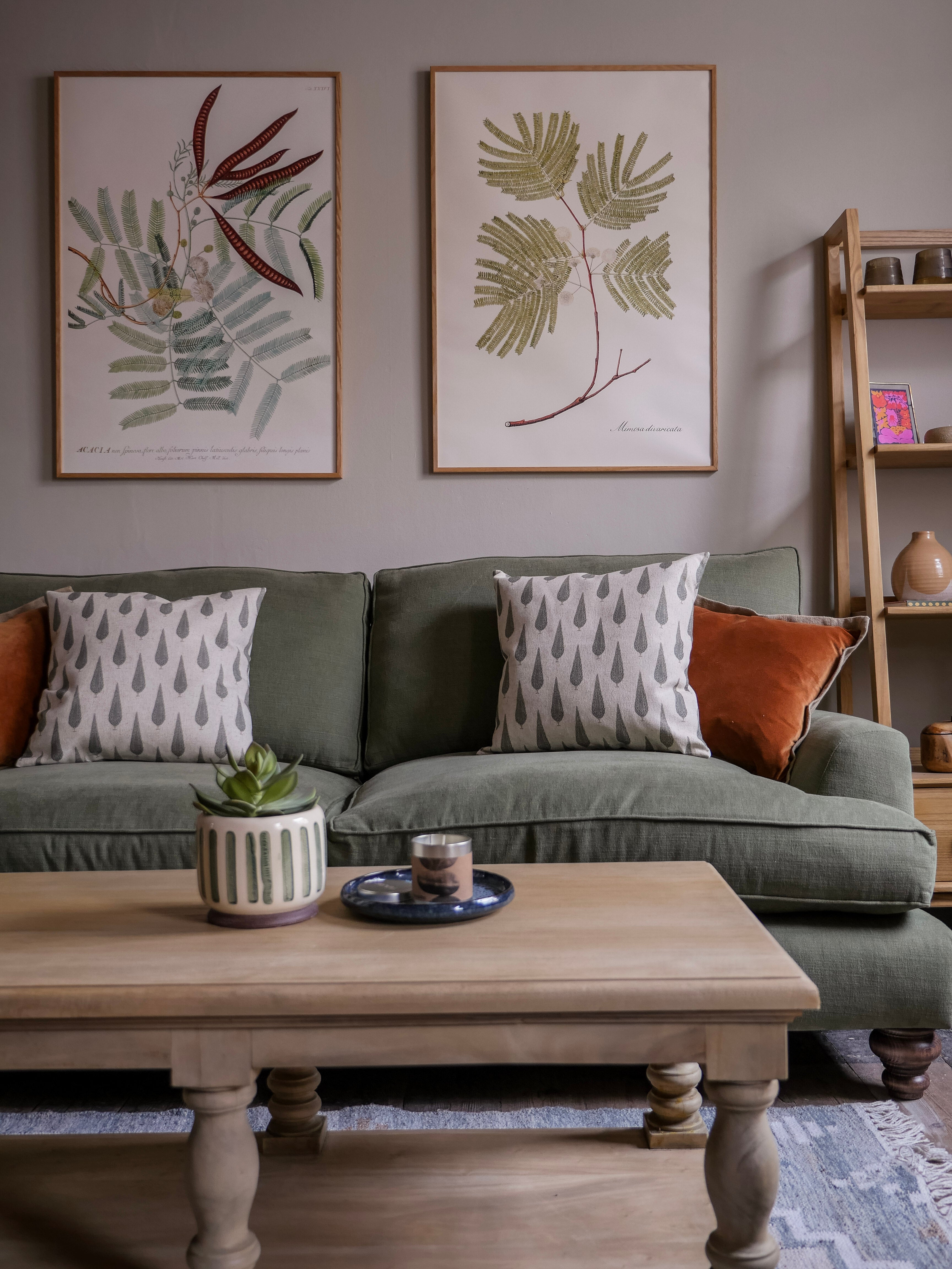 Living room with a green Paulus & Brown bespoke sofa, vintage wooden coffee table, and botanical wall art.