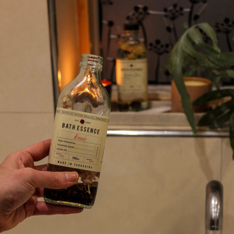 Uneeka Team members hand holding a bottle labeled 'Rose Bath Essence' in a bathroom setting.