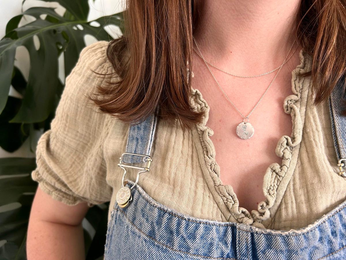 Person wearing a beige top and denim overalls with a sterling silver necklace, standing against a neutral background.