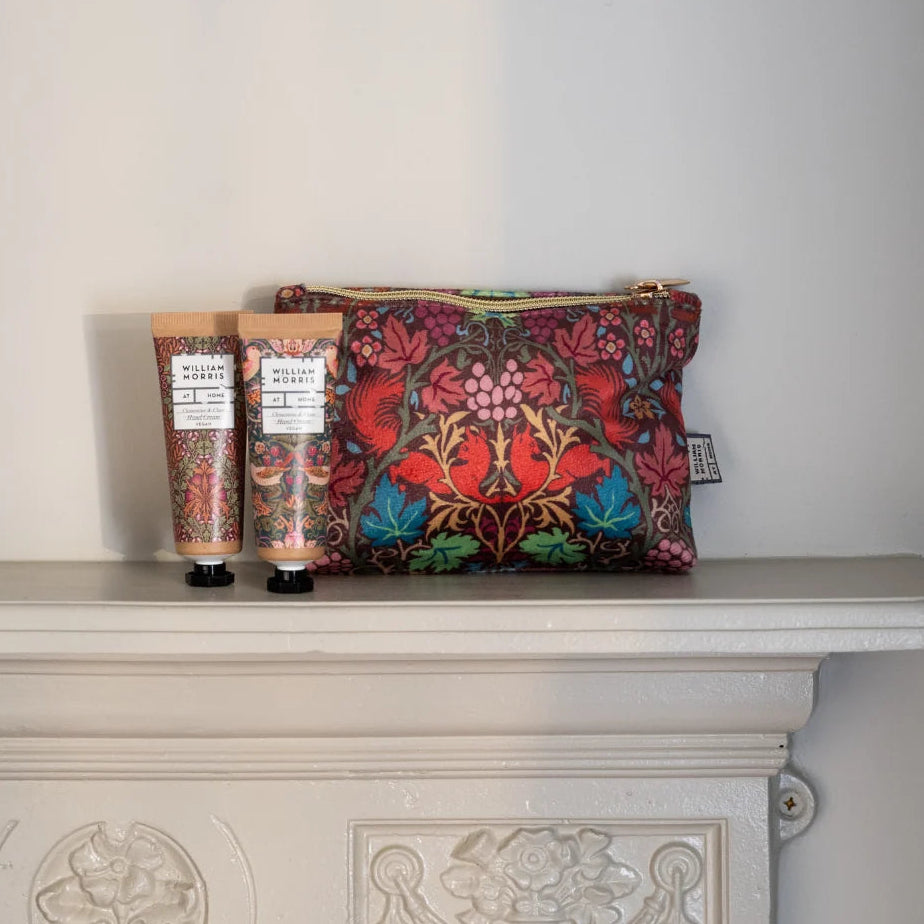 A floral toiletry pouch and two matching hand cream tubes with white labels sit on a white fireplace mantel against a plain light wall.