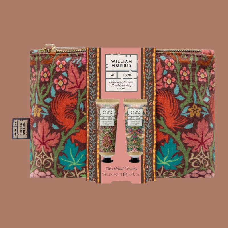 William Morris 'At Home' hand care gift set featuring a floral patterned zip pouch and two hand cream tubes on a solid brown background.