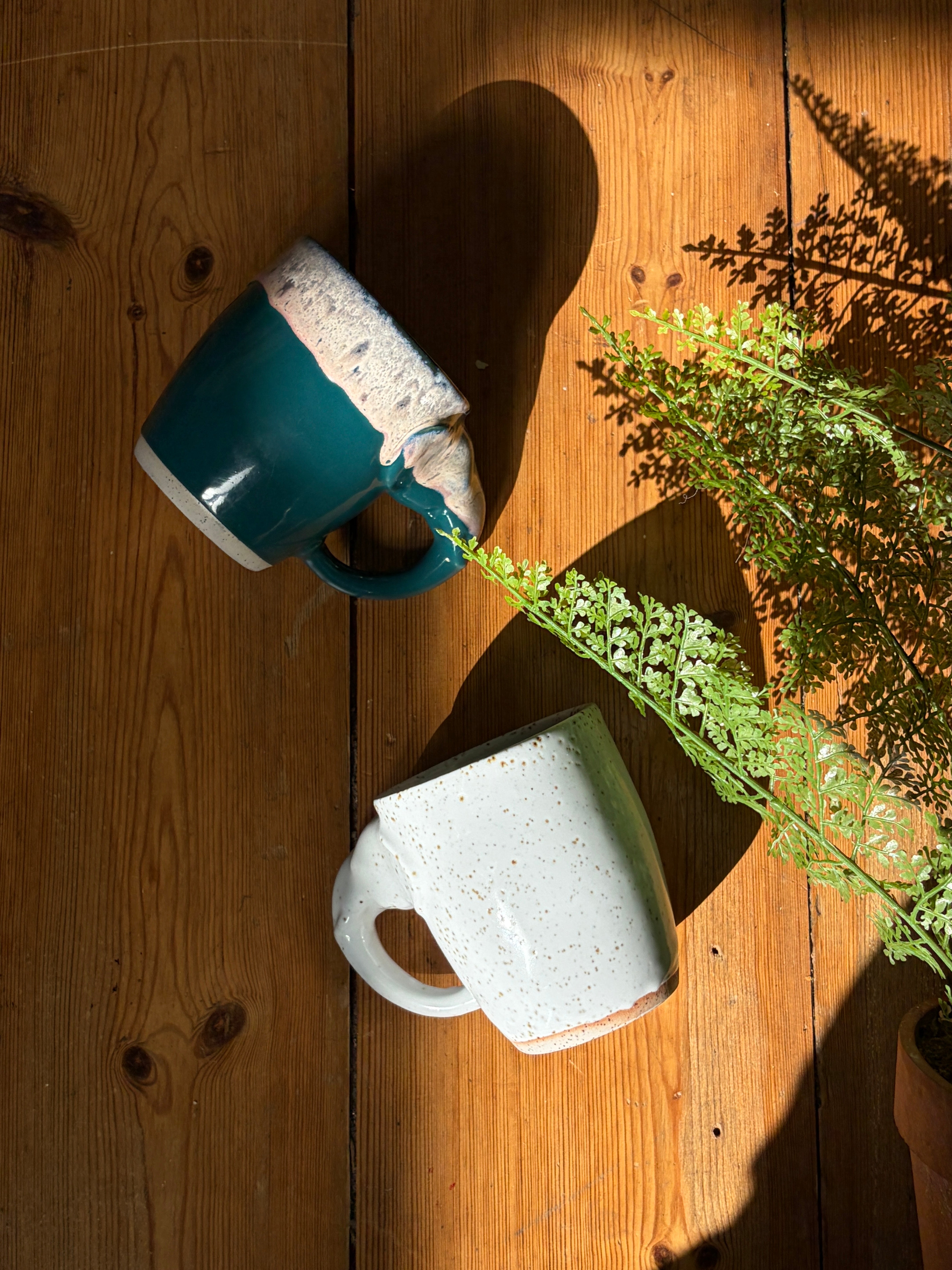 Two ceramic mugs on a wooden tabletop in dramatic sunlight: 