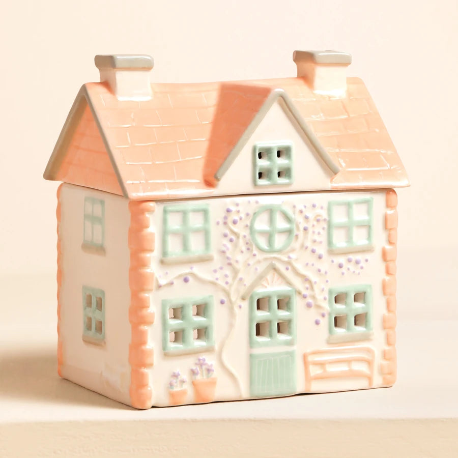 A ceramic decorative house with a peach-coloured tiled roof, cream-colored walls, and pastel green window frames, set against a soft beige background 83062 Uneeka