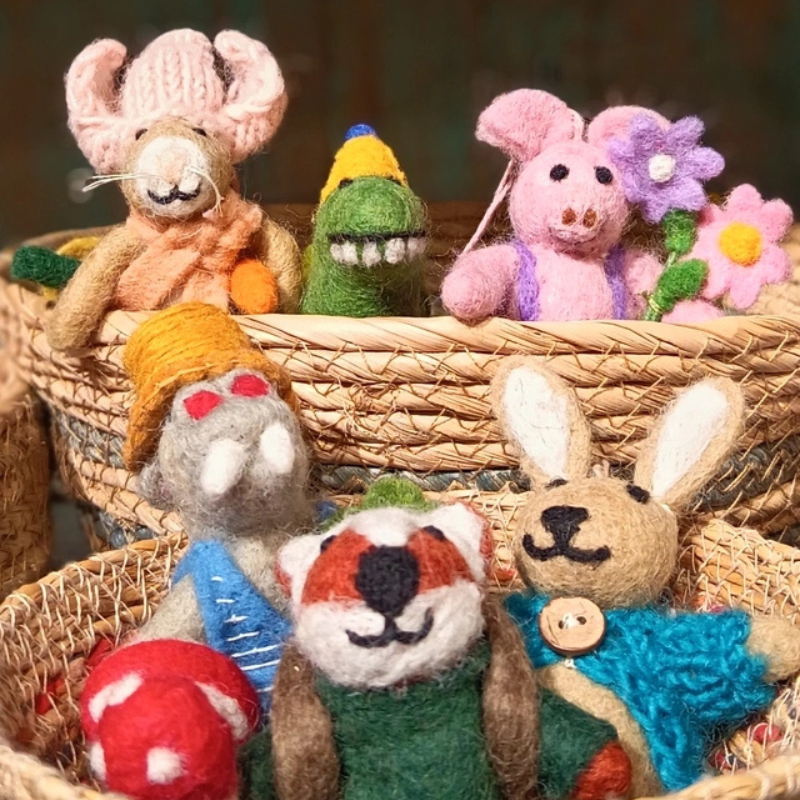 A group of handcrafted felt animal and nature decorations arranged in woven baskets, including a bunny, dinosaur, pig, hippo and fox