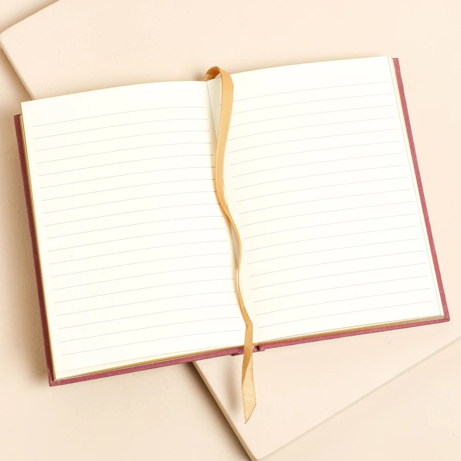 'Thoughts & Daydreams Journal' An open lined notebook with cream pages and a tan ribbon bookmark, resting on a beige background 79566 Uneeka