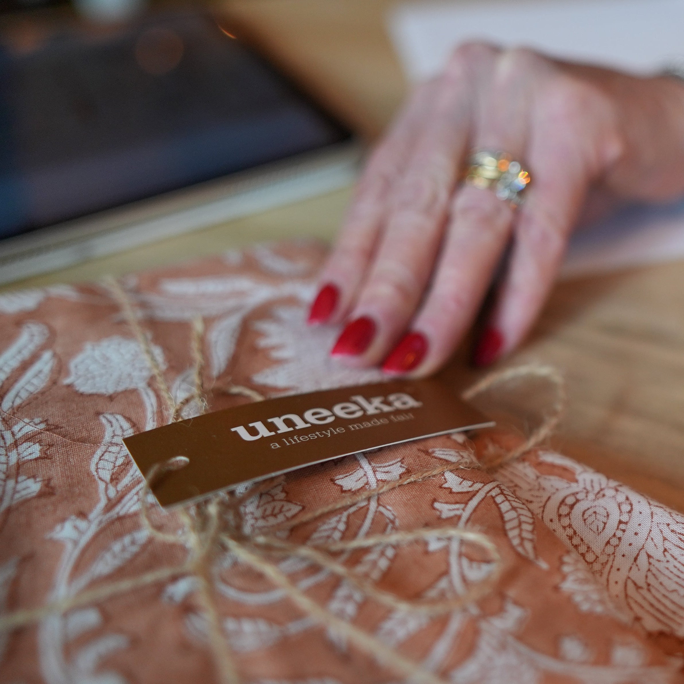 Hand with red nail polish holding a 'uneeka' tag on a patterned fabric background