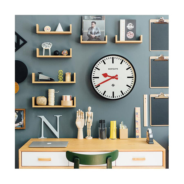 A large black station wall clock with a bold marker dial, contrasting red hands and deep straight-cut metal case with a gloss black finish